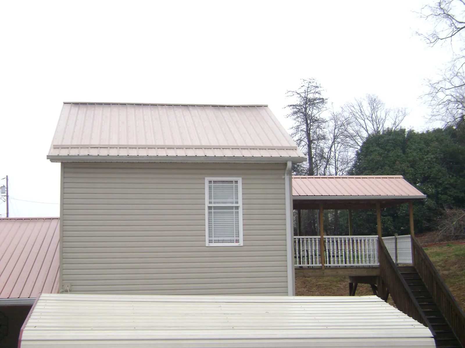 Tan metal roofs on a two story addition and attached porch, from a Roof Replacement job in Dudley